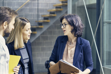 Businesswomen and man discussing paperwork in open plan office - CUF09194