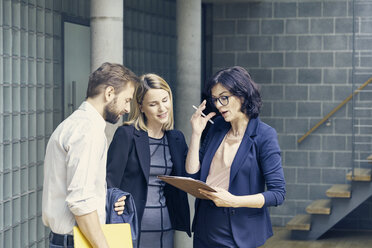 Businessman and women discussing paperwork in open plan office - CUF09196