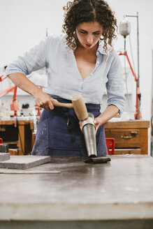 Female jeweller hammering bangle at workbench - CUF09238