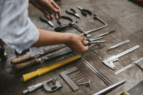 Hände einer Juwelierin beim Auslegen von Handwerkzeugen an einer Werkbank in einer Schmuckwerkstatt, lizenzfreies Stockfoto