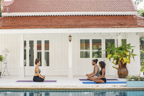 Zwei Frauen und ein Mann üben Yoga am Pool - MOMF00426