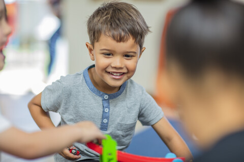 Fröhlicher Junge spielt mit anderen Kindern im Kindergarten, lizenzfreies Stockfoto