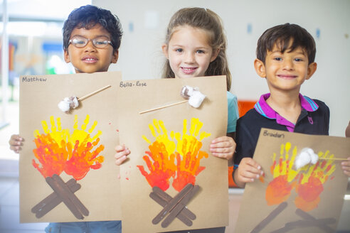 Porträt von lächelnden Kindern, die Bilder von Feuer im Kindergarten präsentieren - ZEF15453