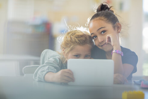 Porträt von zwei lächelnden Mädchen, die sich ein Mini-Tablet im Kindergarten teilen - ZEF15461