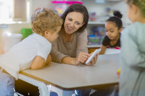 Vorschullehrerin zeigt Kindern im Kindergarten ein Mini-Tablet, lizenzfreies Stockfoto