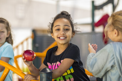 Porträt eines glücklichen Mädchens, das im Kindergarten einen Apfel isst, lizenzfreies Stockfoto