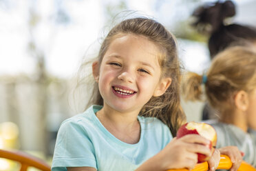 Porträt eines glücklichen Mädchens, das im Kindergarten einen Apfel isst - ZEF15472