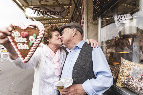 Senior couple with gingerbread heart kissing on fair stock photo