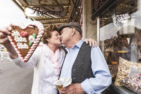 Senior couple with gingerbread heart kissing on fair - UUF13737