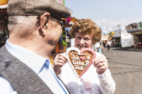 Portrait of hasmiling senior woman presenting gingerbread heart on fair - UUF13738