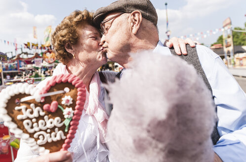 Senior couple with gingerbread heart and cotton candy kissing on fair - UUF13739