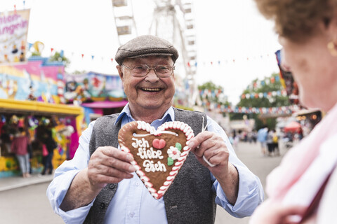 Portrait of happy senior man presenting gingerbread heart on fair stock photo