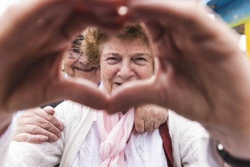Porträt einer glücklichen älteren Frau, die mit ihren Händen ein Herz formt - UUF13744