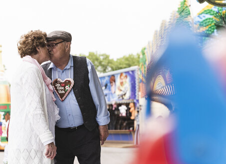 Senior couple with gingerbread heart kissing on fair - UUF13749