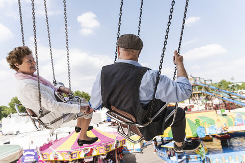 Senior couple hand in hand on chairoplane at funfair - UUF13756