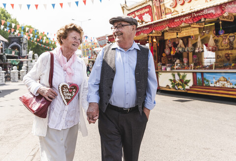 Happy senior couple walking hand in hand on fair stock photo