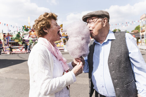 Seniorenpaar auf dem Jahrmarkt, das gemeinsam Zuckerwatte isst - UUF13759