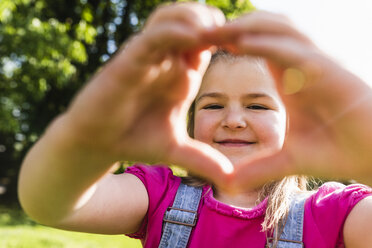 Portrait of smiling girl shaping a heart with her hands in park - UUF13761