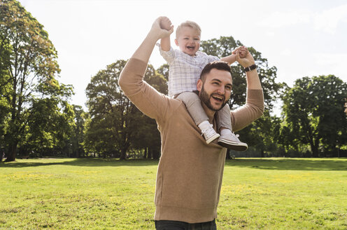 Happy father carrying son on shoulders in a park - UUF13779