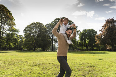 Happy father carrying son on shoulders in a park - UUF13780
