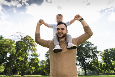 Happy father carrying son on shoulders in a park - UUF13781