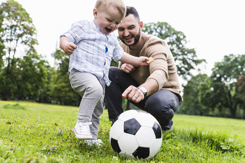 Happy father playing football with son in a park stock photo