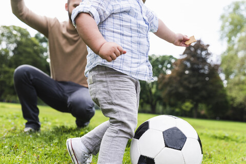 Glücklicher Vater spielt mit seinem Sohn im Park Fußball, lizenzfreies Stockfoto