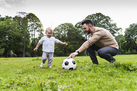 Glücklicher Vater spielt mit seinem Sohn im Park Fußball, lizenzfreies Stockfoto