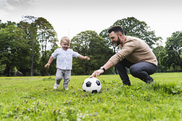 Happy father playing football with son in a park - UUF13785