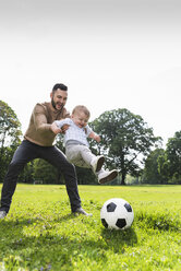 Happy father playing football with son in a park - UUF13787
