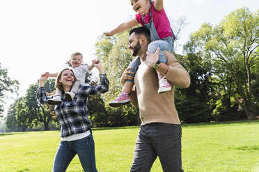 Happy parents carrying children on shoulders in a park - UUF13789