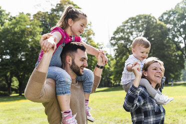 Glückliche Eltern tragen ihre Kinder auf den Schultern in einem Park - UUF13790