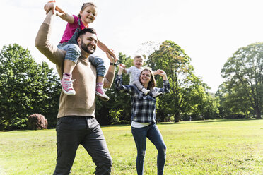 Happy parents carrying children on shoulders in a park - UUF13791