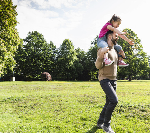 Glücklicher Vater trägt Tochter auf den Schultern in einem Park, lizenzfreies Stockfoto