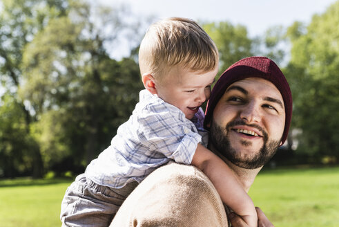 Glücklicher Vater trägt seinen Sohn auf den Schultern in einem Park - UUF13794