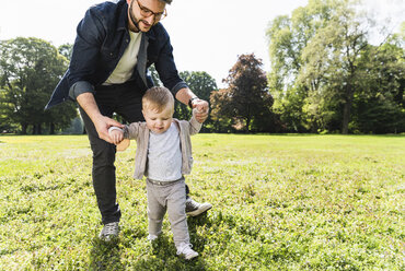 Vater hilft seinem Sohn beim Spazierengehen in einem Park - UUF13803