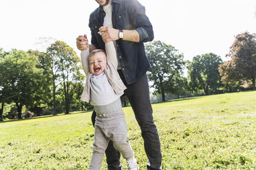 Father holding hands of happy son in a park - UUF13805