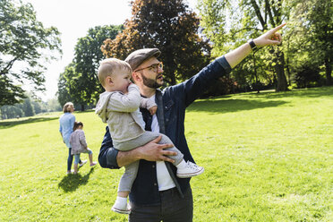 Father carrying and talking to son in a park - UUF13813