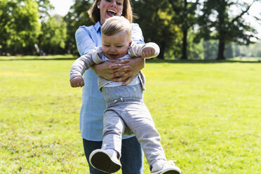 Happy mother lifting up son in a park - UUF13815