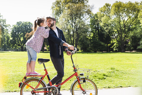 Tochter küsst Vater mit Fahrrad in einem Park, lizenzfreies Stockfoto