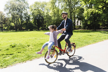 Glücklicher Vater, der mit seiner Tochter in einem Park Fahrrad fährt - UUF13818