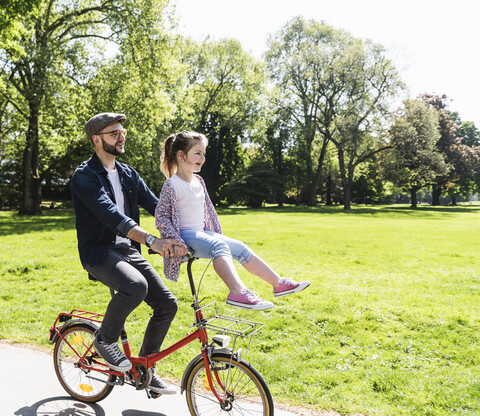 Glücklicher Vater auf dem Fahrrad mit Tochter auf dem Lenker sitzend in einem Park, lizenzfreies Stockfoto