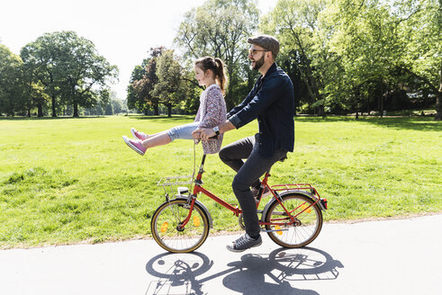 Happy father riding bicycle with daughter sitting on handlebar in a park - UUF13820