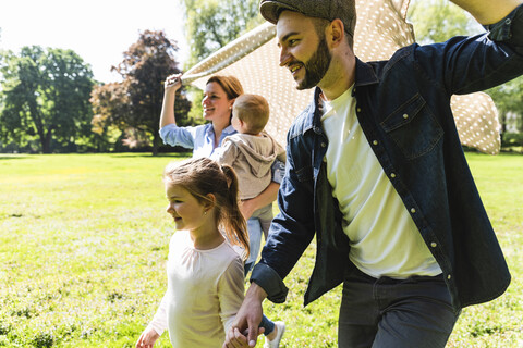 Glückliche Familie, die mit einer Decke in einem Park spazieren geht, lizenzfreies Stockfoto