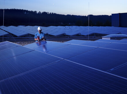 Worker with measuring device checking solar plant in the evening - CVF00536