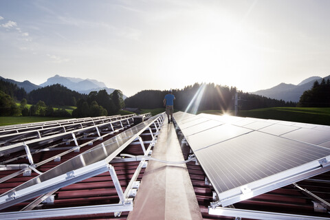 Österreich, Tirol, Kössen, Rückenansicht eines Arbeiters, der abends auf eine Solaranlage läuft, lizenzfreies Stockfoto