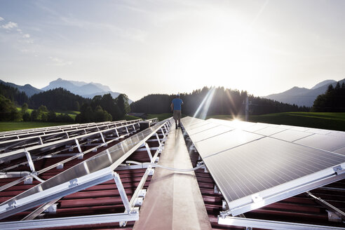 Österreich, Tirol, Kössen, Rückenansicht eines Arbeiters, der abends auf eine Solaranlage läuft - CVF00537