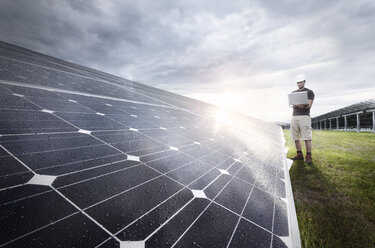 Ingenieur mit Laptop bei der Kontrolle einer Solaranlage in der Abenddämmerung - CVF00539