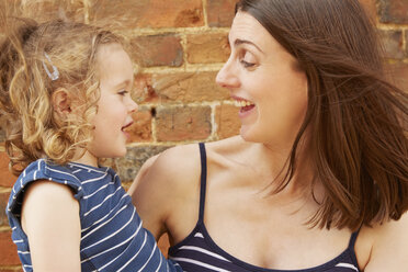 Cute girl and laughing mother by brick wall - CUF09279