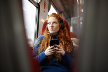 Woman on train listening to music on mobile phone with headphones, London - CUF09292